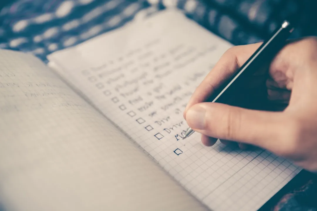 A hand writing a checklist with a pen in a spiral notebook