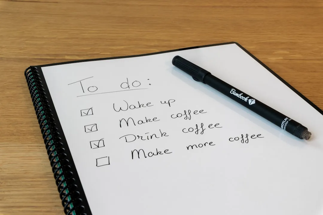 A handwritten to-do checklist in a notebook next to a marker pen on a wooden desk