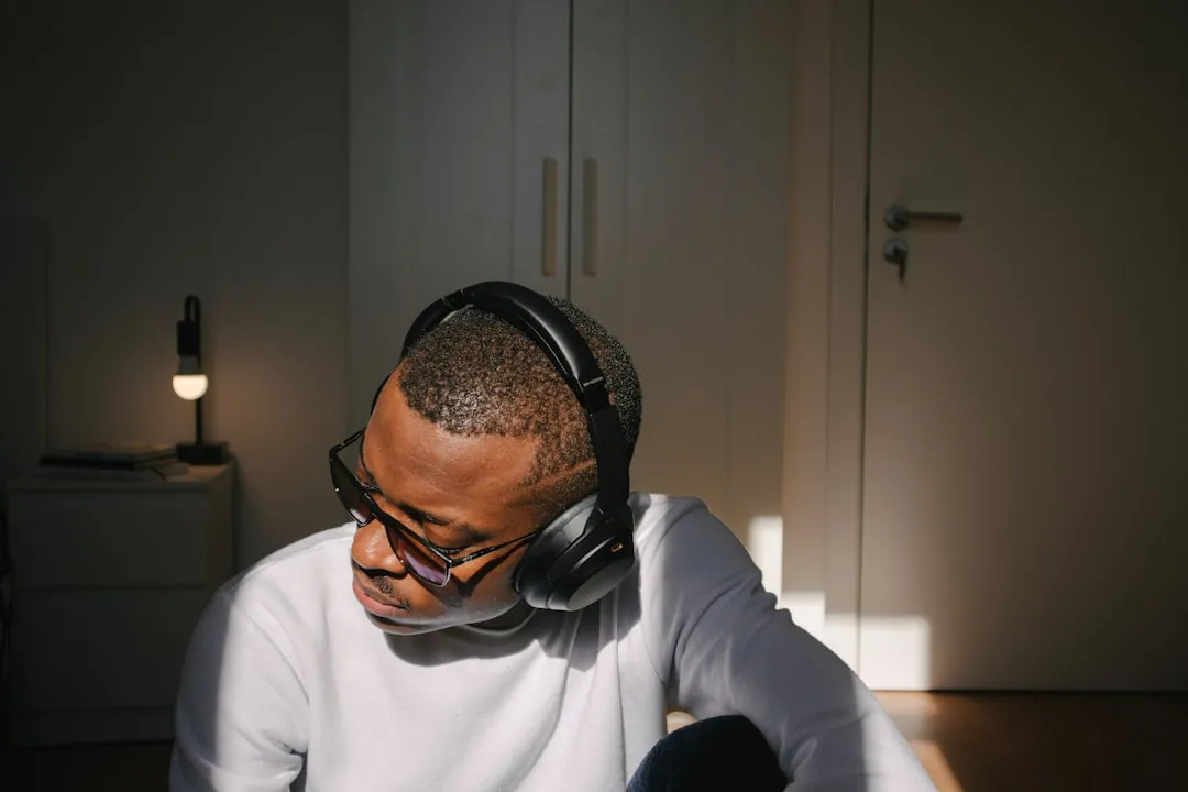 A man wearing over-ear headphones and sunglasses sitting in a sunlit room