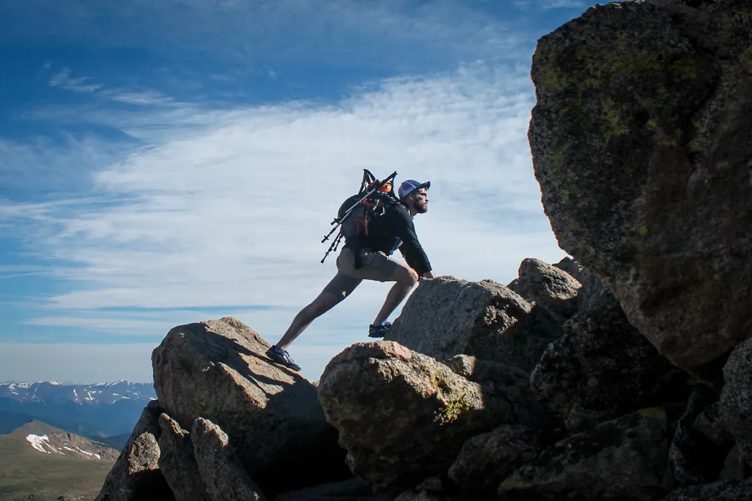 A hiker with a backpack climbing over large boulders on a mountain ridge
