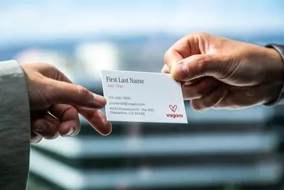 Two hands passing a business card between them, the card printed with placeholder text reading “First Last Name”