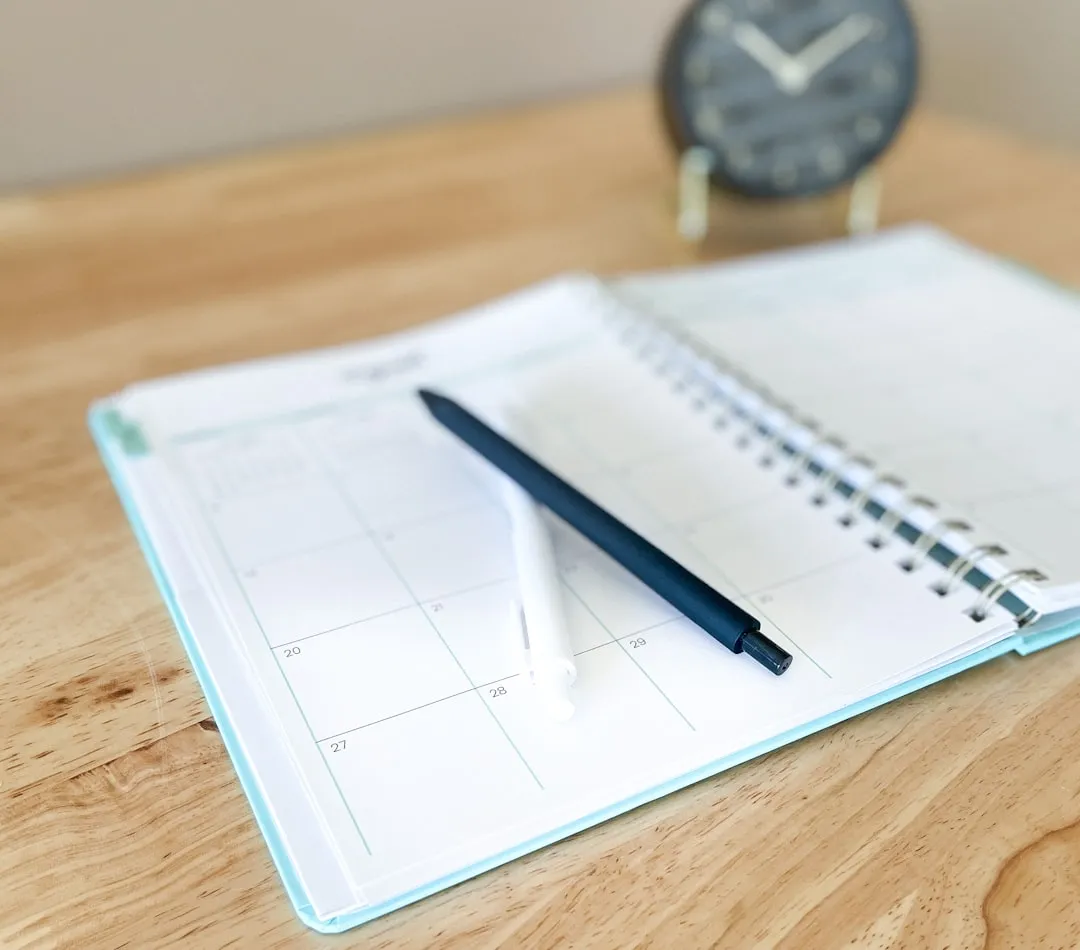 An open planner with a pen on a wooden desk.
