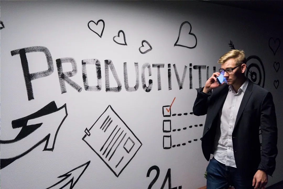 A man on his phone standing in front of a wall painted with "Productivity" graffiti art