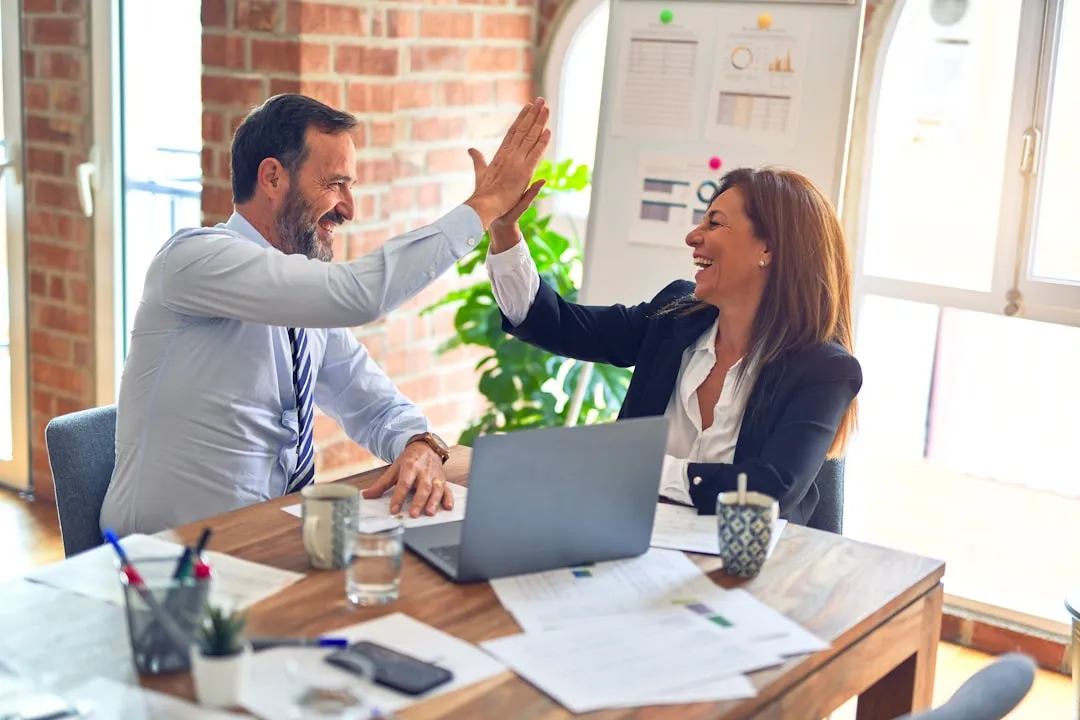 Two coworkers high-fiving over a laptop at a desk