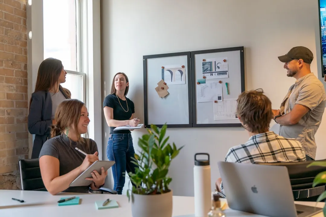 A team of five colleagues reviewing project boards in an office while one presents