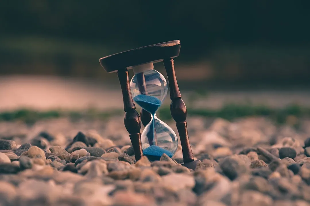 An hourglass with blue sand standing on a bed of pebbles