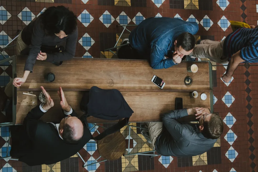 Overhead view of four people leaning over a table talking, with phones and coffee cups on the table