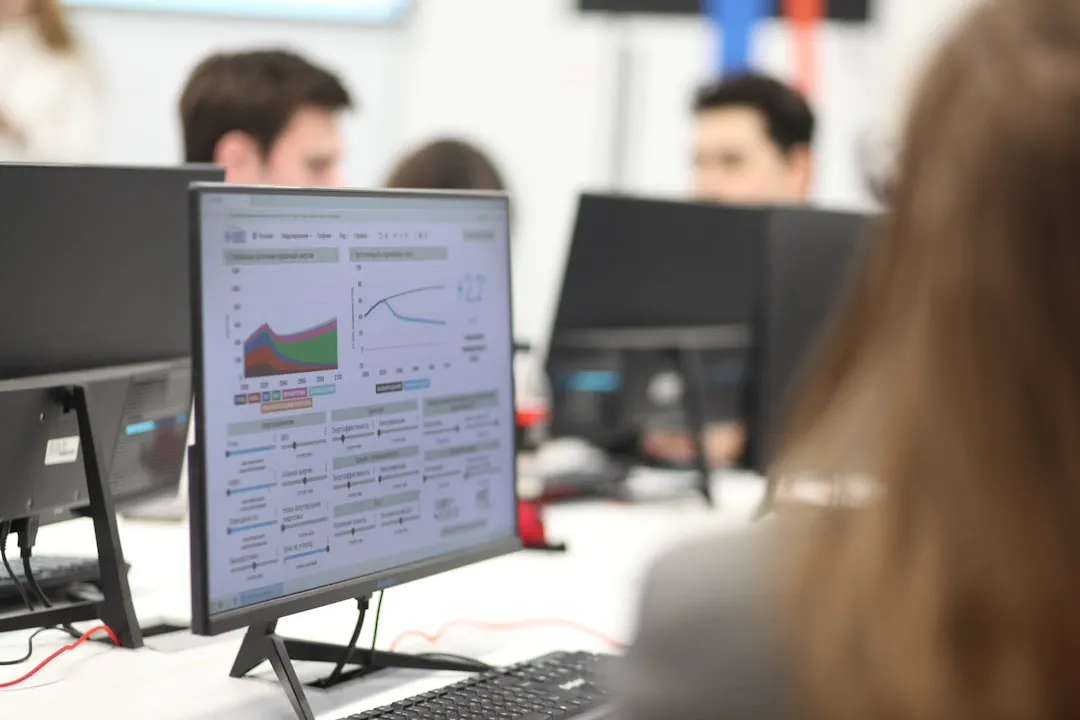 A computer monitor displaying colorful analytics dashboard charts, with coworkers in the background