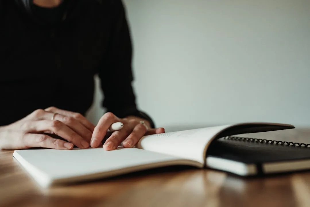 Close-up of hands resting on an open blank notebook on a desk