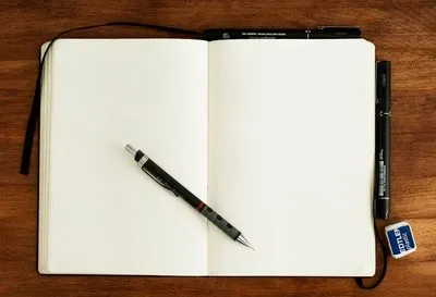 An open notebook lying flat on a wooden desk with a mechanical pencil resting on the blank page