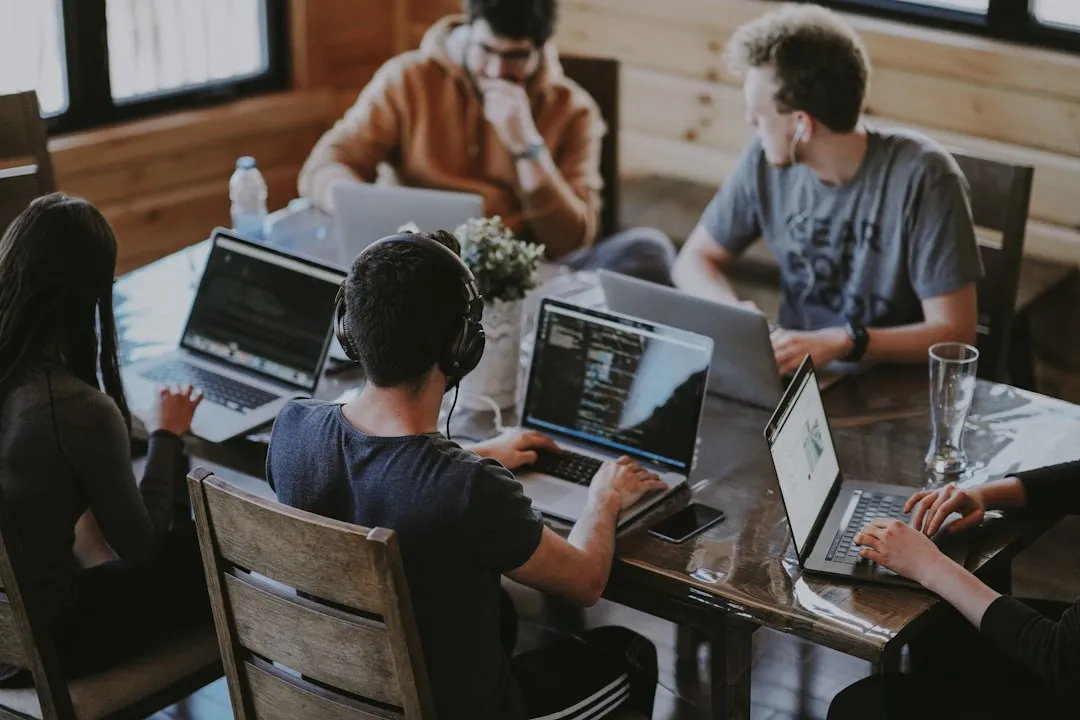 A group of coworkers working on laptops around a wooden table