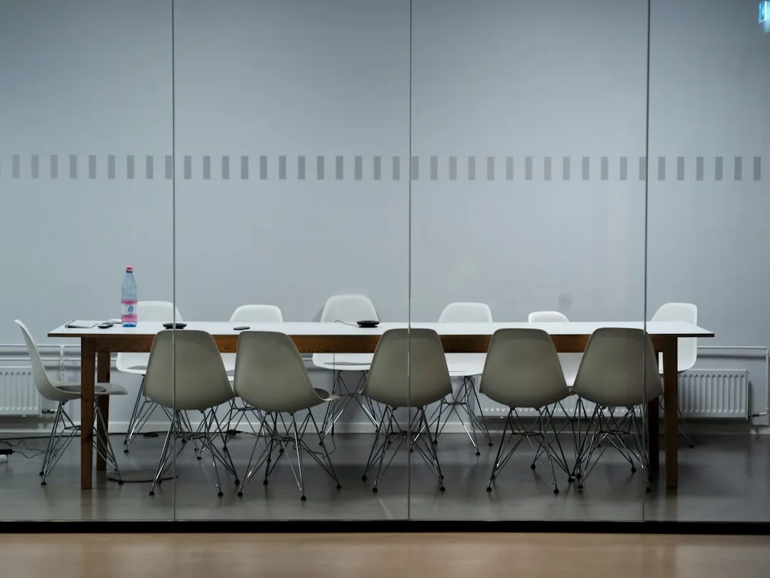 An empty glass-walled conference room with a long table and chairs