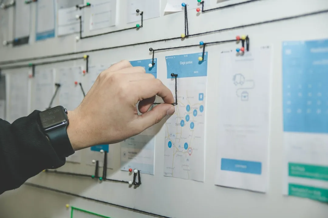 A hand pinning a printed mobile app mockup to a wall-mounted project planning board with string and pins